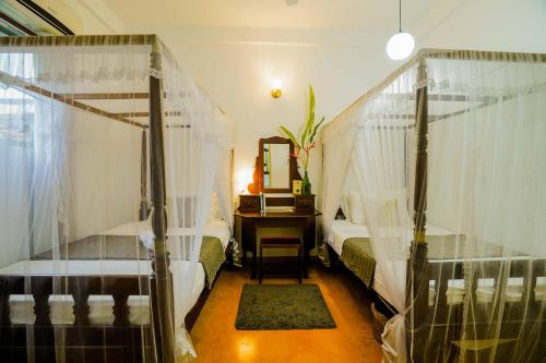a bedroom with two beds and a desk with a mirror at Fort Dew Guest House in Galle