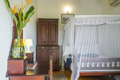a bedroom with a bed with a white curtain and a table at Fort Dew Guest House in Galle