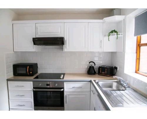a kitchen with white cabinets and a sink at Pebble Cottage, Cromer in Cromer