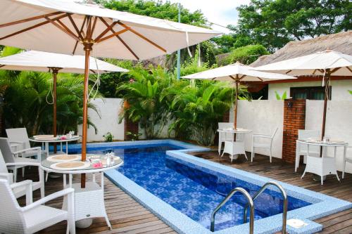 a patio with tables and umbrellas and a pool at Burudika Bungalows in Selong Belanak