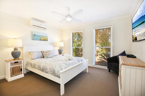 a white bedroom with a bed and two windows at Calming Waters - Pet Friendly - Community Pool in Callala Beach