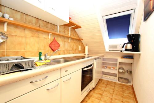 eine Küche mit weißen Schränken, einem Waschbecken und einem Fenster in der Unterkunft Grote in Hörnum