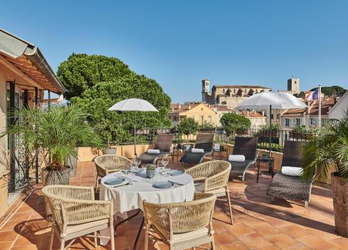 um pátio com uma mesa, cadeiras e guarda-sóis em Hotel Le Suquet Cannes em Cannes