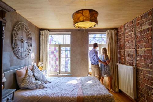 Ein Mann und eine Frau stehen in einem Schlafzimmer mit Blick aus dem Fenster in der Unterkunft Gîtes d'Apothecarius entre Namur et Dinant in Fosses-La-Ville