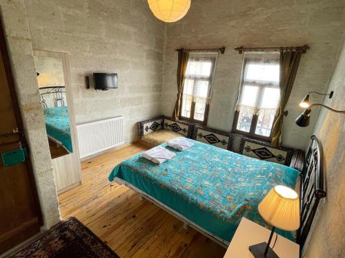 a bedroom with a bed with a blue comforter and two windows at Karadut Cave Hotel in Göreme