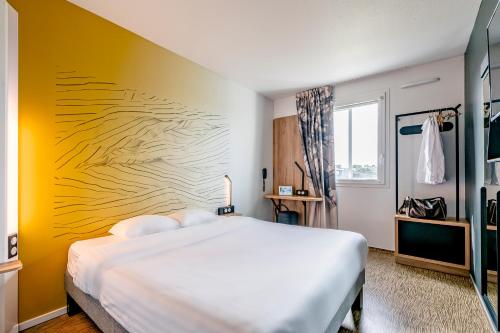 1 dormitorio con cama blanca y pared amarilla en B&B HOTEL Bordeaux Talence, en Gradignan