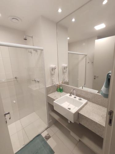 uma casa de banho branca com um lavatório e um chuveiro em Apart Hotel - América Residence Campos dos Goytacazes em Campos dos Goytacazes