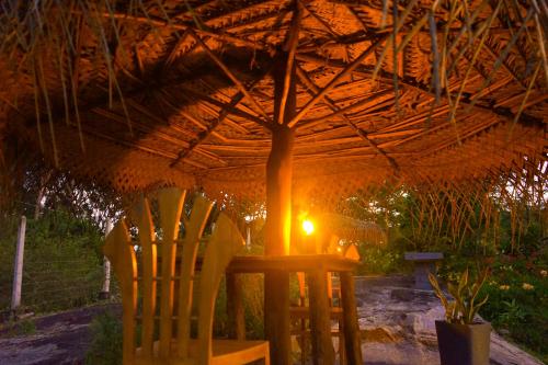 a table and a chair under a straw umbrella at Hidden Lake Cottages Sigiriya in Sigiriya