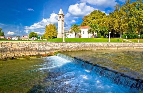 a river with a stone wall and a clock tower at Apartment "Dida" with Free Private Parking in Solin