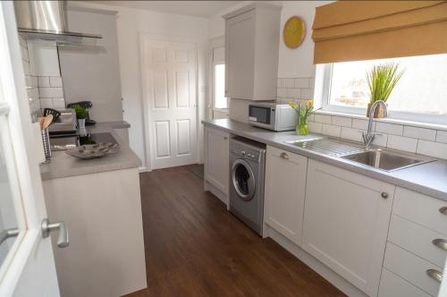 a white kitchen with a sink and a dishwasher at The Mila - Ayr Racecourse - Coorie Doon Stays in Ayr