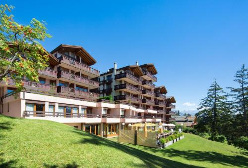 a large apartment building on a hill with a green field at Aparthotel Helvetia in Crans-Montana