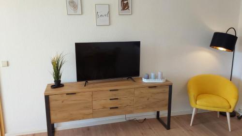 a television on a wooden dresser with a yellow chair at Komfortables Apartment in Bad Elster mit Netflix in Bad Elster
