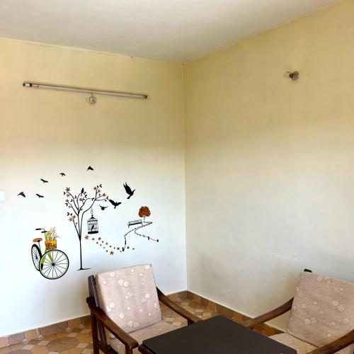 a room with two chairs and a wall with a tree and birds at Anand Niketan Homestay Shimla in Shimla