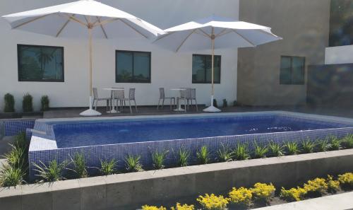 una piscina con 2 sombrillas, mesas y sillas en HM HOTEL EXPRESS en Colima