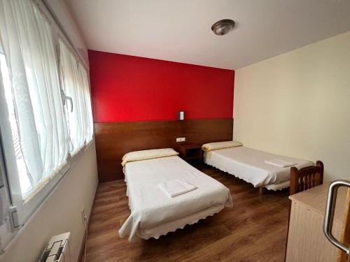 a room with two beds and a red wall at Pensión Carballeira in Arzúa