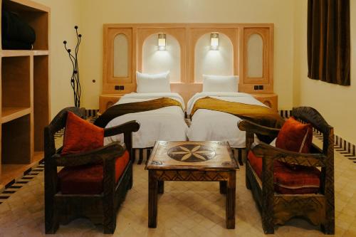 a bedroom with two beds and two chairs and a table at Dar Marhaba Merzouga in Merzouga