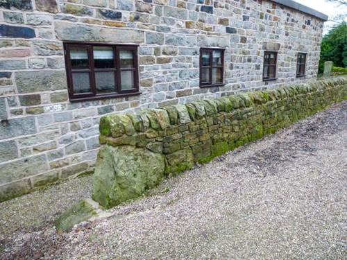 una pared de piedra junto a un edificio de ladrillo en Moorlands Farm Cottage en Foxt