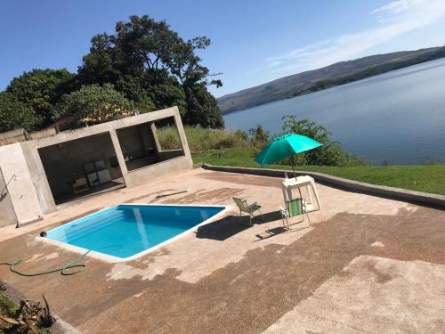 a swimming pool with an umbrella next to a body of water at RANCHO SAPUCAÍ in Passos
