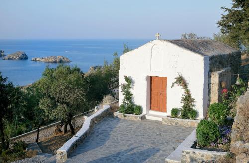 a small white building with a red door on a hill at Melenos Art Boutique Hotel in Líndos
