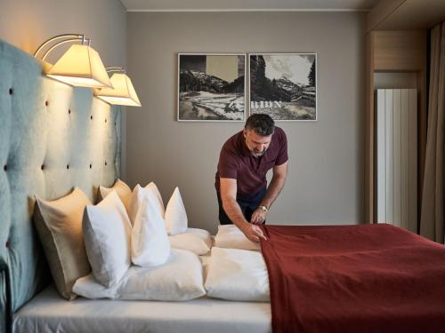 a man arranging pillows on a bed in a hotel room at aja Bergresort Werfenweng in Werfenweng