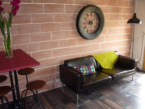 a leather couch against a brick wall with a clock at La Fontaine des Noyers in Saint-Saturnin-les-Apt