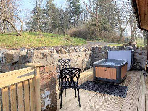 a patio with a grill and two chairs on a wooden deck at Partridge Lodge with Hot Tub in Forgandenny