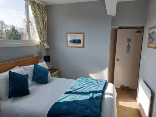 a bedroom with a bed with blue pillows and a window at Invergarry Room Only Guest House For Adults in Windermere