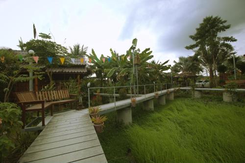 a wooden walkway in a garden with benches and plants at เรือนไทยใจสุขเอ๋ย in Ban Bang Wa