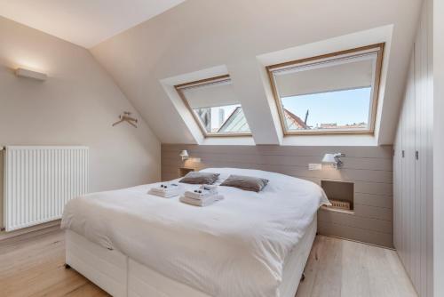 a bedroom with a large white bed with two windows at Duplex apartment with terrace - next to the beach in Knokke-Heist