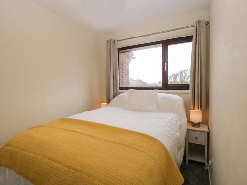 a bedroom with a bed with a yellow blanket and a window at Wren Cottage in Weymouth