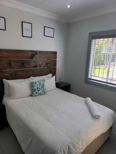 Schlafzimmer mit einem großen weißen Bett mit einem Kopfteil aus Holz in der Unterkunft Triple9 Hatfield Guesthouse in Pretoria