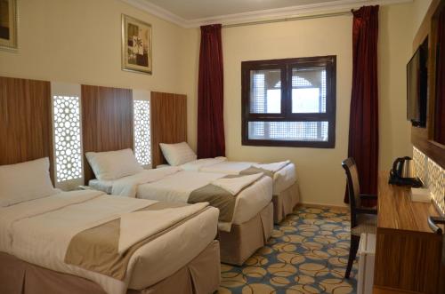 a hotel room with three beds and a window at Artal Al Alami Hotel in Al Madinah