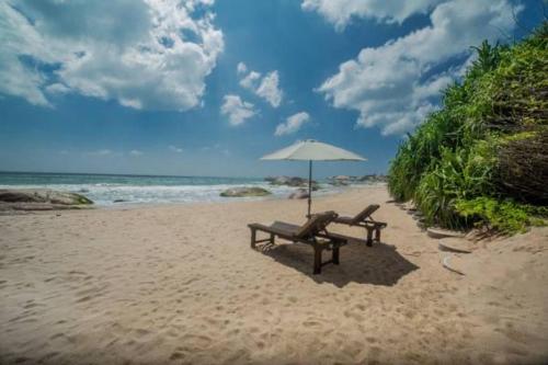 a bench and an umbrella on a beach at NIKARA Luxury Beach House in Tissamaharama