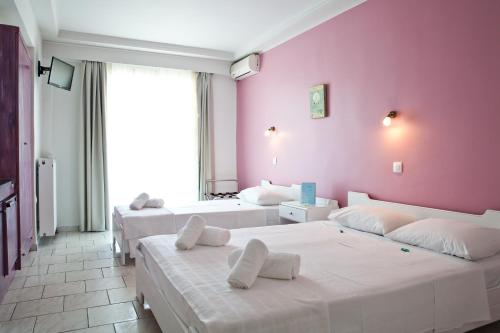 1 dormitorio con 3 camas y pared de color rosa en Hotel Melissanthi, en Paralia Dionisiou