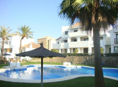 uma piscina com um guarda-sol e duas palmeiras em Islantilla Bajo con Jardin na Islantilla