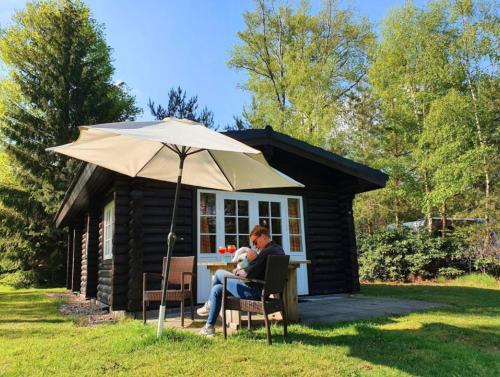 a man sitting at a table in front of a cabin at Scandinavian Lodges (by Outdoors Holten) in Holten