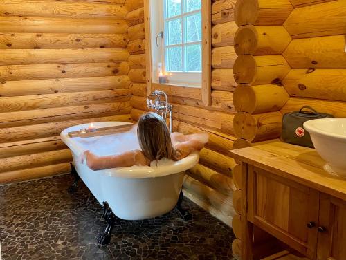 una persona sdraiata in una vasca da bagno in un bagno in legno di Scandinavian Lodges (by Outdoors Holten) a Holten