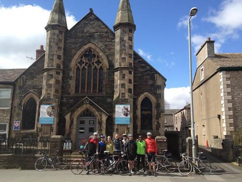 un grupo de gente parada frente a una iglesia con sus bicicletas en Kirkby Stephen Hostel, en Kirkby Stephen