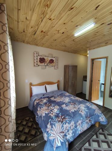 Ce lit se trouve dans une chambre dotée d'un plafond en bois. dans l'établissement chales e aptos Carvalhos em monte verde, à Monte Verde