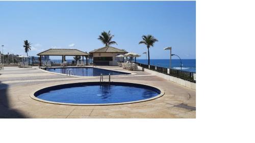 una piscina junto a una playa con palmeras y el océano en Marazú OndinaApart, en Salvador