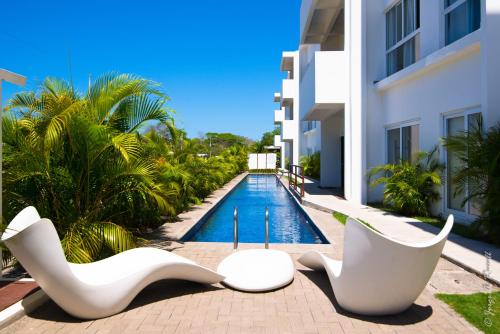 a swimming pool with white chairs next to a building at Jaco Modern & Beach Apartment - Lapa Living A1 in Jacó