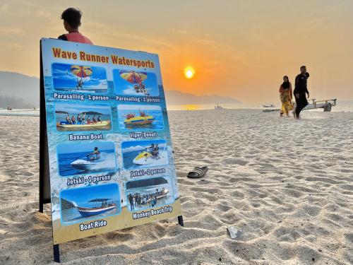 a sign on the beach with people watching the sunset at By The Sea, Penang in Batu Ferringhi
