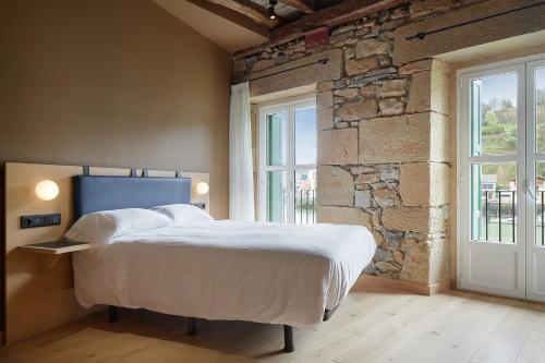 1 dormitorio con 1 cama grande y pared de piedra en Donibanea, en Pasajes de San Juan