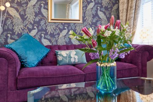 a vase of flowers on a glass table with a purple couch at The Granville - Delightful 2-bed Victorian Apartment in Harrogate