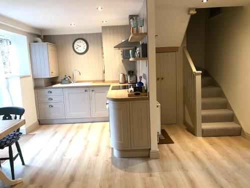 een keuken met een wastafel en een trap met een klok bij STABLES Stylish comfortable peaceful cottage with parking and outdoor space in Holt