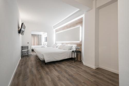 a white bedroom with two beds and a window at Hotel Sansi Park in Lleida