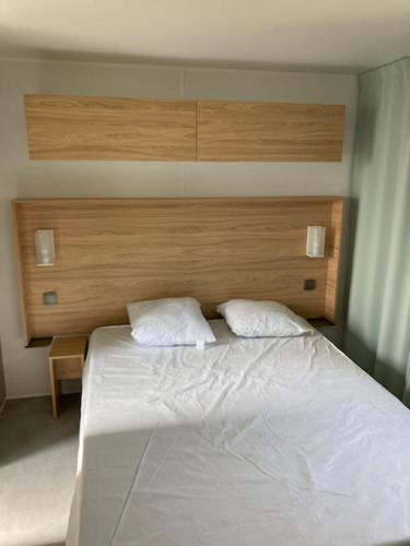 une chambre avec un lit blanc avec une tête de lit en bois dans l'établissement MOBIL HOME 8 PERSONNES 2 SALLES DE BAIN 40 m2 HAUT STANDING, à Aureilhan