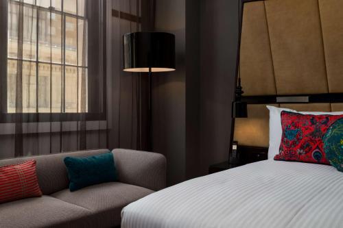 a bedroom with a bed and a couch and a window at QT Sydney in Sydney