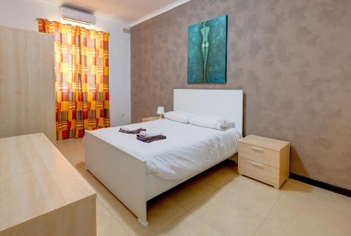 ein Schlafzimmer mit einem weißen Bett und einem Gemälde an der Wand in der Unterkunft Modern 2 Bedroom Maisonette in Central Sliema in Sliema