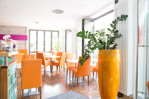 a restaurant with orange chairs and a vase with a plant at Hotel Arooma in Erding